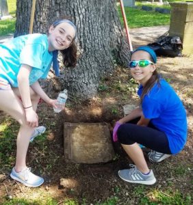 Girl Scouts Katie Patterson and Layla Walker uncover broken headstone during cleanup day at Town Cemetery Saturday
