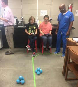 School Board member Shaun Tubbs observes students in the DCHS media center/library/ makerspace operating robots Linda and Terry from Ipads. The robots can be made to talk, move their heads, and move across the floor. The demonstrations show students how robotics can be used for fun as well as for industrial use in factories.