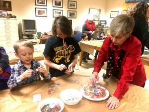 Christmas on the Square 2018: Kathy Hendrixson of Justin Potter Library showing Will and Faith Tripp how to make a Christmas ornament.