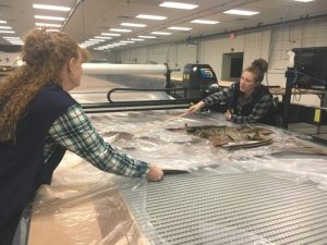 Employees Sandy Sexton (left) and Rebekah West of 620 Pelham, Inc (formerly Omega Apparel) operating an automated cutter where the garments are cut, stamped, and bundled before delivery to the sewing department across the street.