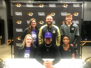 DCHS football athlete Tyzaun Ladet signed with Bethel University at McKenzie to play outside linebacker. He was joined at the announcement by family and friends: Seated left to right: Talon Billings, Tyzaun Ladet, Cyerra Ladet (sister). Standing left to right: Allie Lasser, Assistant Tiger Coach Corey Rathbone, and Kobbe Clary
