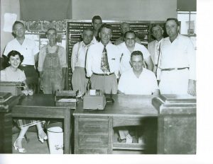 Sue Nixon Puckett worked as Deputy Clerk for County Clerk Sam Love in the early 1950’s. Photo from 1953 or 54 shows them seated at the table and desk. First standing row left to right: County Judge Homer Murphy and Sheriff C.H. Malone. Second standing row left to right: Superintendent of Schools Roe Harney, Courthouse Janitor Ridley Ledbetter, Clerk and Master Bethel Foster, and Register of Deeds George Waggoner. Third row standing left to right: Trustee Aubrey Turner, Circuit Court Clerk Jim Roy, and General Sessions Judge T.M. Yeargin.