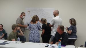 Members of the redistricting committee looking over county map showing the existing seven districts and the proposed changes