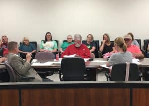 Director of Schools Patrick Cripps (seated left with back to camera) presents 2024-25 school budget to county budget committee with teachers seated along the wall behind the committee