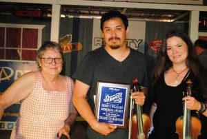 Tyler Andal of Nashville has repeated as the Smithville Fiddlers Jamboree Fiddle-Off Champion . Kim Luton, President and Coordinator of the Festival presented the award to Andal at 12:15 a.m. Sunday morning. Also pictured is Bonnie Norris of Nashville (right) the Senior Fiddling Champion who was edged out by Andal , the Junior Champion, in the Fiddle-Off